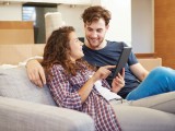 Couple Relaxing On Sofa With Digital Tablet In New Home