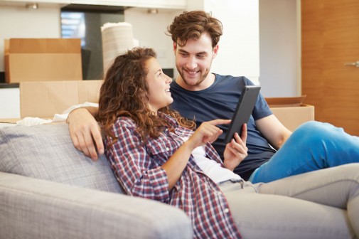 Couple Relaxing On Sofa With Digital Tablet In New Home